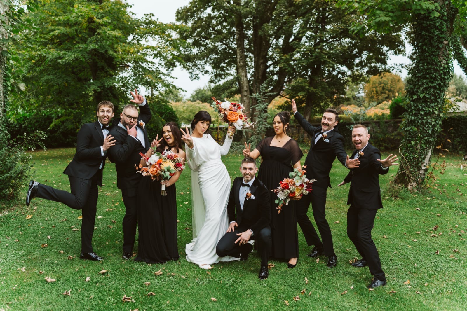 Wedding party posing outdoors with greenery in the background